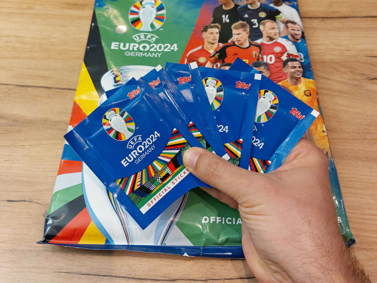 Hand hält mehrere Packungen Euro 2024 Sticker vor dem offiziellen Album